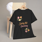 Black t-shirt with 'Spring Into Gardening' text and floral designs on a wooden chair.