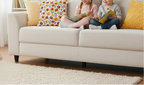 Two children sitting on a beige sofa with colorful pillows, reading books.