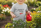 Child in a garden wearing a 'Gardener in Training' shirt, holding a red watering can.