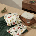 A pair of cream-colored pants with an all-over Christmas tree pattern in red, green, and gold, displayed flat against a light beige background.