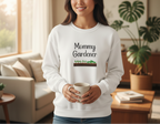 Woman wearing a white sweatshirt with 'Mommy Gardener' text, holding a cup in a living room.