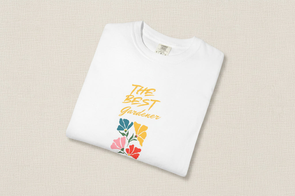 White t-shirt with 'The Best Gardener' text and floral designs on a beige background