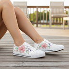 White sneakers with floral designs worn by a person sitting on a wooden deck.
