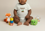 Baby wearing a onesie with text and graphics, surrounded by toys on a beige background