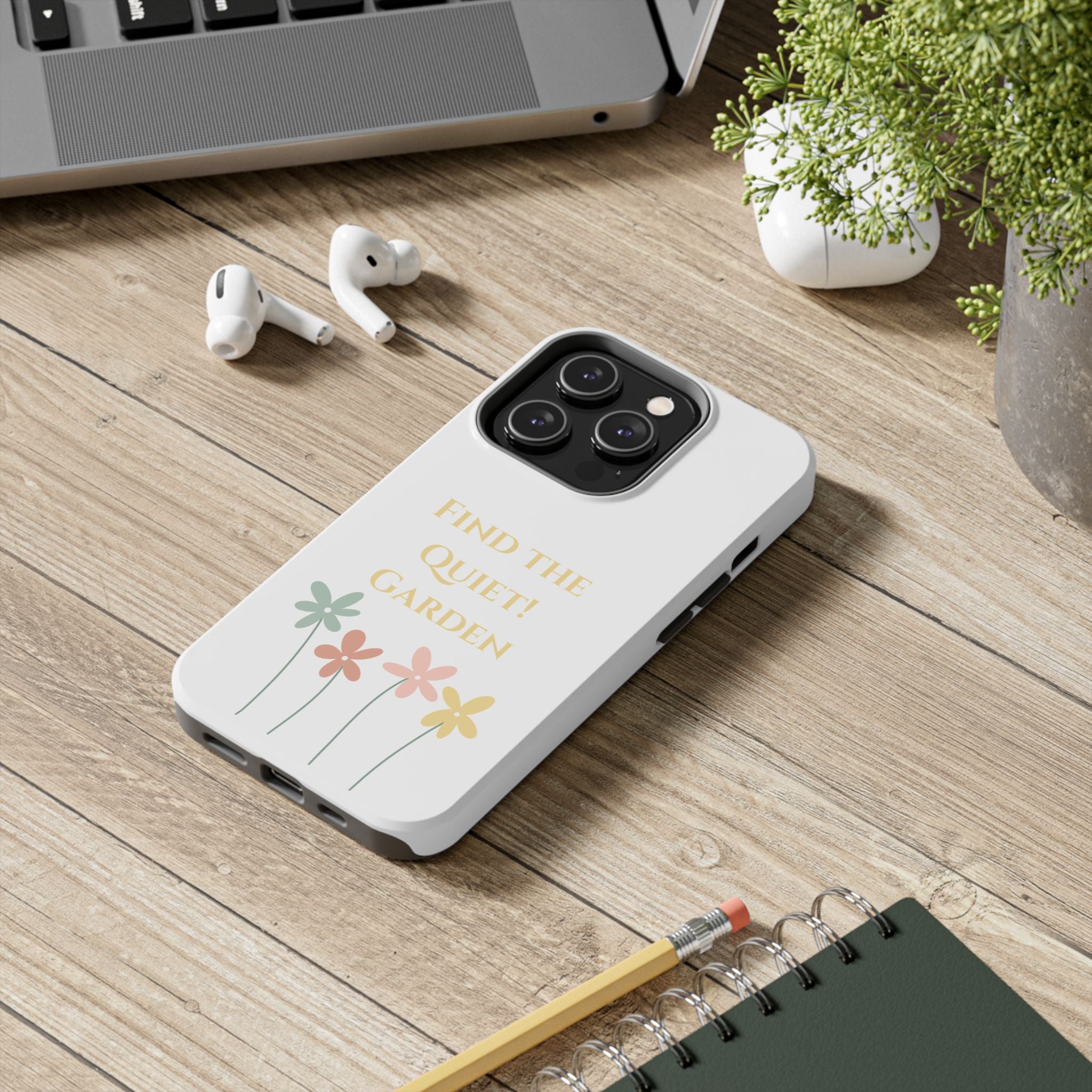 White phone case with text on a wooden surface with laptop, earbuds, and notebook.