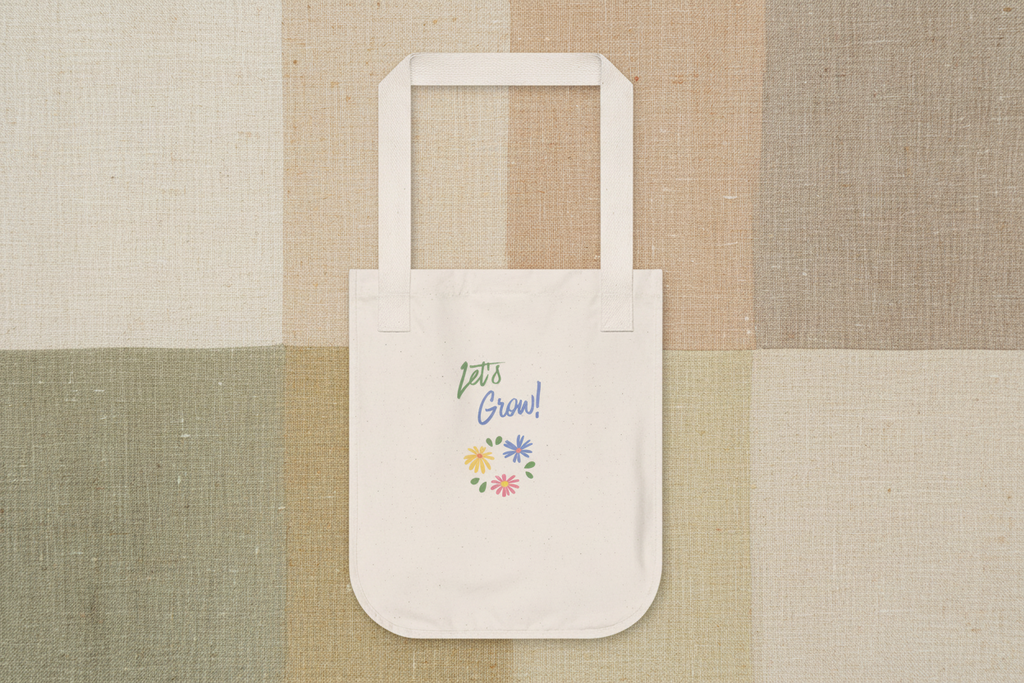 A cream canvas tote bag with white handles, featuring a colorful graphic that reads 'Let's Grow!' in green and blue script with small yellow, blue, pink, and purple flowers. The bag is centered on a textured patchwork background of beige, tan, and sage green linen-like panels.