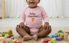 Baby in a pink 'Baby Gardener' onesie surrounded by toys on a carpeted floor.