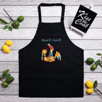Black apron with graphic design on a wooden surface with lemons and limes.