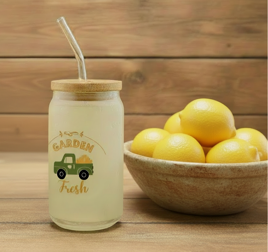 Jar with 'Garden Fresh' label and straw next to a bowl of lemons on a wooden surface
