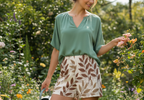 Woman in a garden wearing a green top and leaf-patterned shorts, holding a watering can.