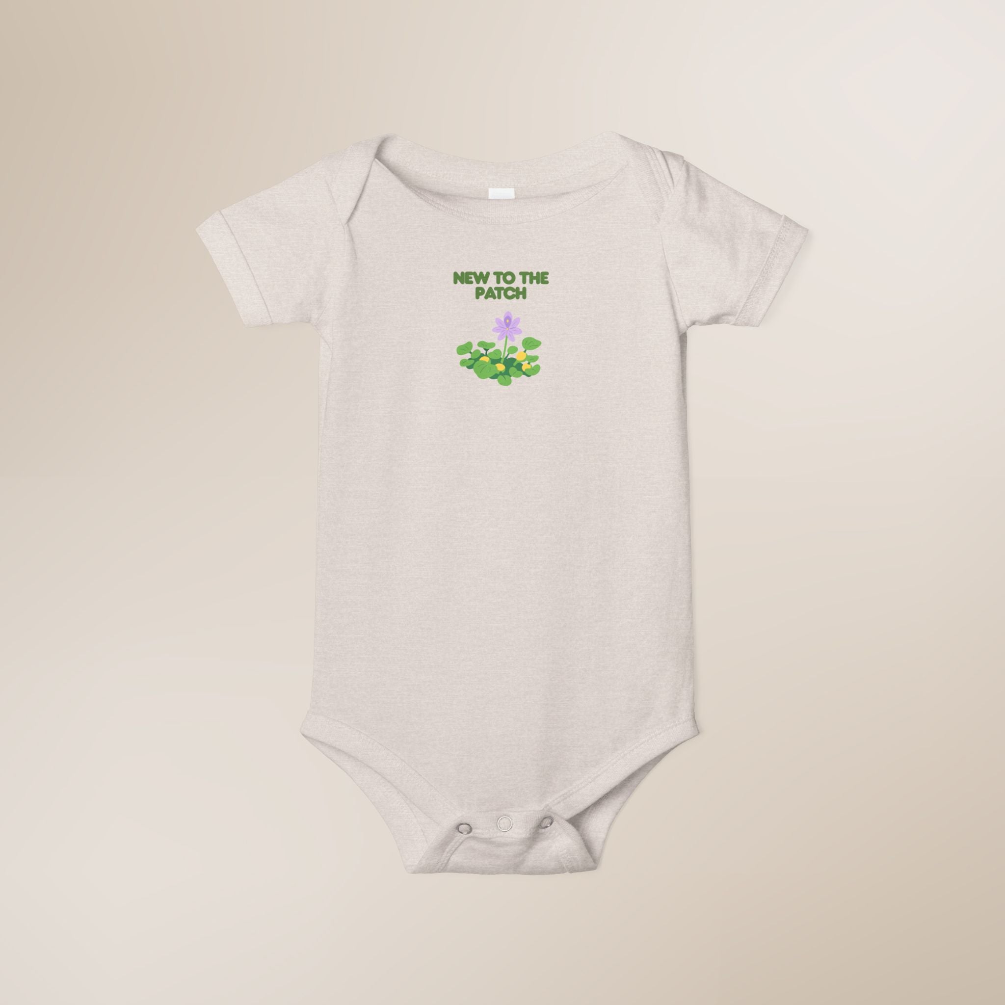 White baby onesie with 'New to the Patch' text and graphic on a beige background