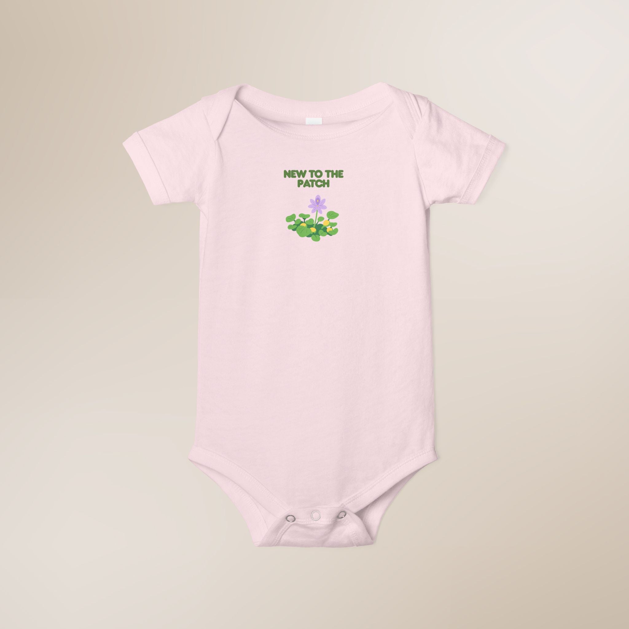 Pink baby onesie with 'New to the Patch' text and graphic on a beige background