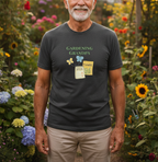 A man wearing a dark gray graphic t-shirt that reads 'GARDENING GRANDPA' with small gardening illustrations, standing in a colorful garden.