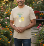 A man wearing a beige graphic t-shirt that reads 'GARDENING GRANDPA' with a seed packet illustration, standing in a lush, colorful garden.