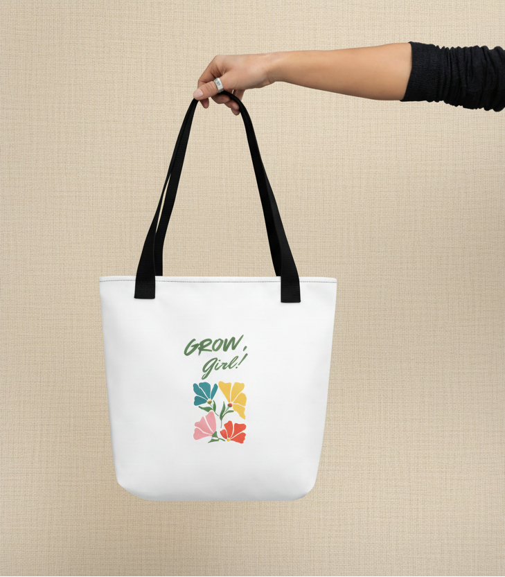 White tote bag with floral design and 'Grow Girl!' text held by a hand against a gray background