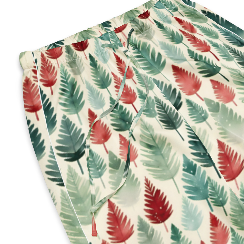 Close-up of a pair of drawstring shorts with an allover tropical leaf print in shades of green, teal, and coral red on a cream background.