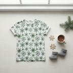 White t-shirt with green snowflake pattern, cup of coffee, and baby shoes on a light surface.