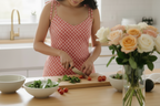 Woman in a kitchen preparing food with a bouquet of flowers on the counter.