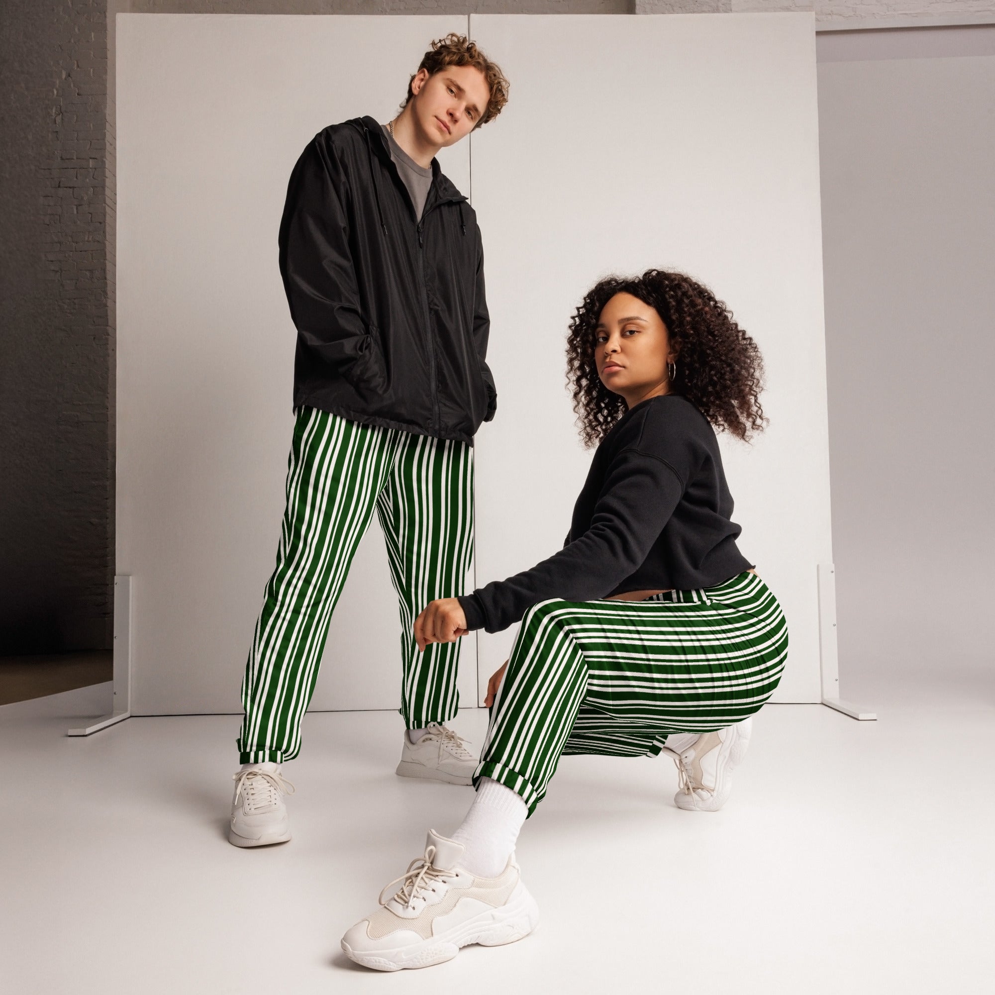 Two people wearing matching green and white striped pants on a plain background