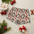 Holiday-themed boxer briefs with a red and green Christmas tree pattern, styled in a cozy flat-lay with a mug of marshmallow hot chocolate, red ornaments, pine branches, cinnamon sticks, and a small gift box.
