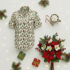 A short-sleeve button-up pajama shirt with a Christmas tree pattern, styled in a flat lay with holiday decorations including poinsettias, gift boxes, candy canes, and a mug of marshmallows.