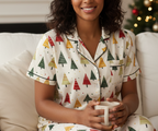 Woman wearing Christmas-themed pajamas holding a mug on a couch.