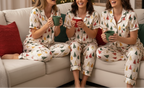 Three women in matching pajamas with a Christmas tree pattern, sitting on a couch and holding mugs.