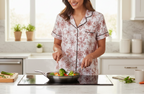 Woman in pajamas cooking vegetables in a pan in a kitchen.