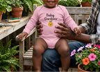 Baby in pink beside greenhouse plants