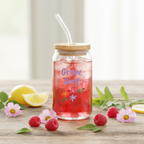 Glass jar with straw and wooden lid filled with red drink, surrounded by raspberries and lemon slices on a wooden surface.