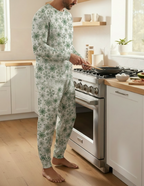 A man wearing a light green and white snowflake-patterned pajama set stands barefoot in a bright kitchen, holding a frying pan near a stainless steel stove.