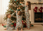 Three children in matching pajamas decorating a Christmas tree in a cozy living room.