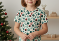 Child wearing a festive shirt with Christmas-themed decorations in a decorated room.