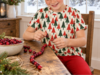 Child in Christmas Tree kids pajama top stringing cranberries at a farmhouse table