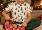 Child wearing a Christmas tree pajama top while opening a wrapped gift