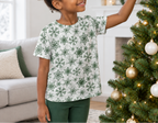 Child wearing green snowflake kids pajama top while decorating a Christmas tree