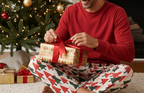 Unique Middle Eastern man wearing Christmas Tree men’s pajama pants with a red shirt while opening a holiday gift