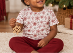 Toddler wearing Red Snowflake kids pajama top holding a wooden snowflake ornament indoors