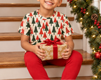 Child in Christmas Tree kids pajama top on a garland staircase holding a present