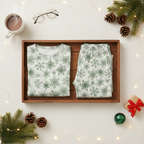 Folded Green Snowflake men’s pajama top and matching smooth pocketless pants in a wooden split tray with cocoa, greenery, gifts, and warm lights