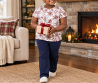 Child wearing Red Snowflake kids pajama top carrying a gift near a fireplace