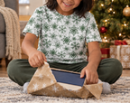 Child wearing green snowflake kids pajama top while opening a gift