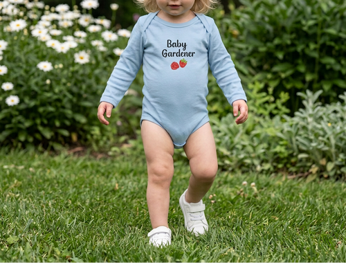 A toddler girl walking on a grassy lawn wearing a light blue long-sleeve bodysuit with 'Baby Gardener' and a small strawberry graphic printed on the chest.