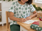 Child wearing green snowflake kids pajama top while writing a holiday card