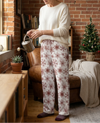 Woman watering a plant wearing Red Snowflake pajama pants and an ivory lounge top