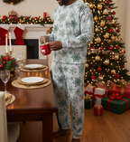 Black man wearing a matching green snowflake long sleeve crew neck pajama set while pouring hot cocoa in a Christmas dining room