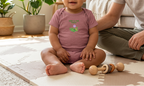 Baby wearing heather mauve New to the Patch flower onesie indoors.