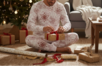 East Asian man in pocket-free red snowflake pajamas wrapping a Christmas gift