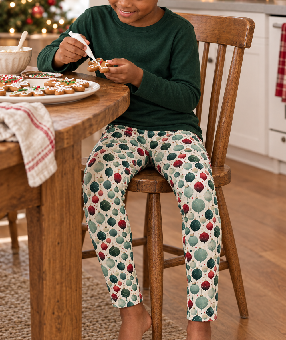 Child wearing Holiday ornament leggings decorating gingerbread in a festive kitchen