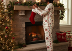Man with locs wearing Christmas Present pajamas while hanging a stocking by the fireplace